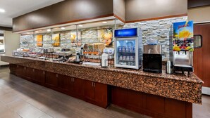 A self-service breakfast bar with a granite countertop, a coffee machine, a juice dispenser, and a refrigerated display case.