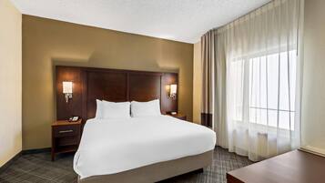 A hotel room with a large bed, two bedside tables with lamps, a wooden headboard, and a window with sheer curtains.
