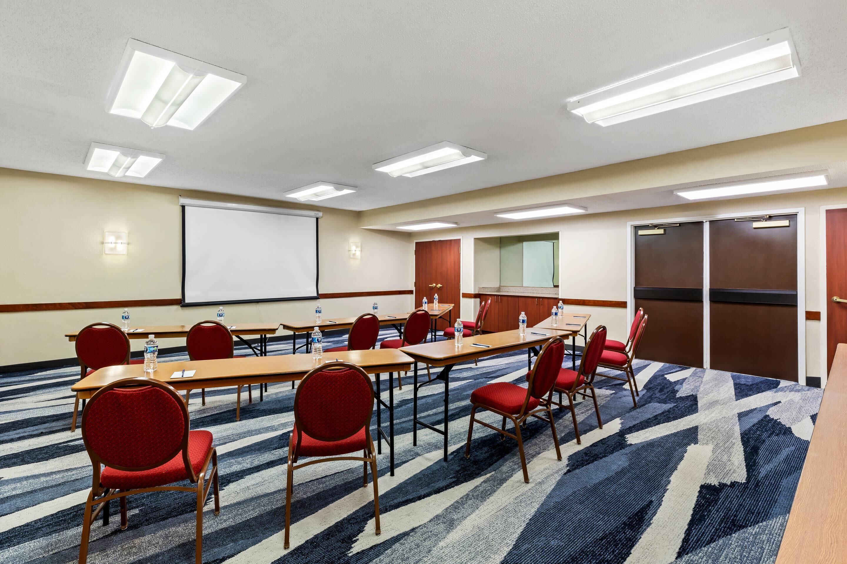 A conference room with a large table, red chairs, and a projector screen.