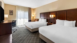 A hotel room with two beds, a desk, a chair, a lamp, and a TV.