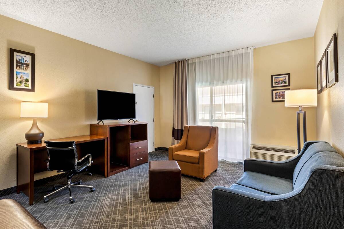A hotel room with a desk, office chair, sofa, and ottoman.