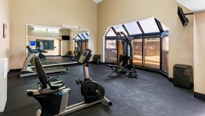 A gym with exercise equipment, a mirrored wall, and large windows.