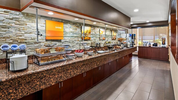 A buffet area with a stone wall backdrop, a sign reading "RISE SHINE," and various food items displayed.
