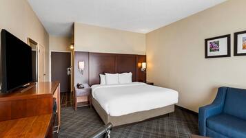 A hotel room with a large bed, a TV, a desk, and a blue armchair.