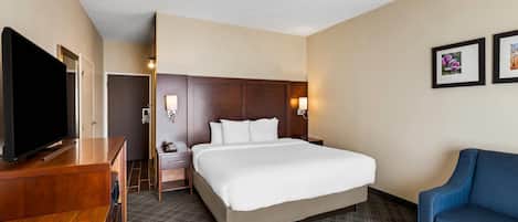 Une chambre d’hôtel avec un grand lit, une télévision, un bureau et un fauteuil bleu.