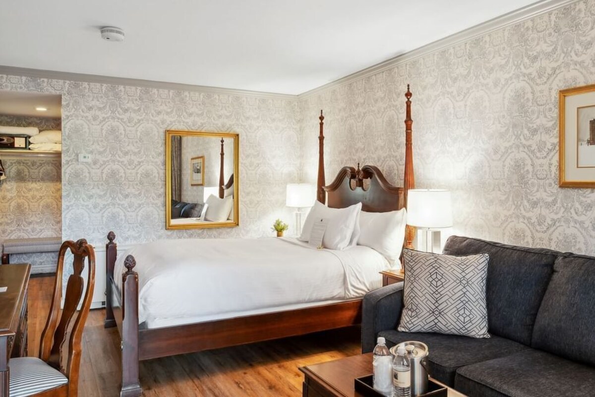 A hotel room with a four-poster bed, a sofa, a desk, and a mirror.