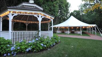 A gazebo and a tent set up in a garden with tables and chairs, surrounded by greenery.