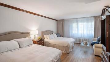 Habitación de hotel con dos camas, un escritorio, una silla y un ventanal con cortinas.