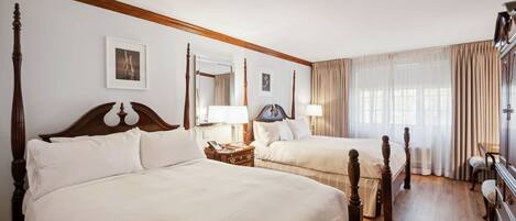 A hotel room with two large beds, wooden headboards, a nightstand, a dresser, and a large window with curtains.