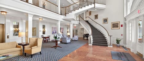 A spacious lobby with a grand staircase, multiple seating areas, and a reception desk.