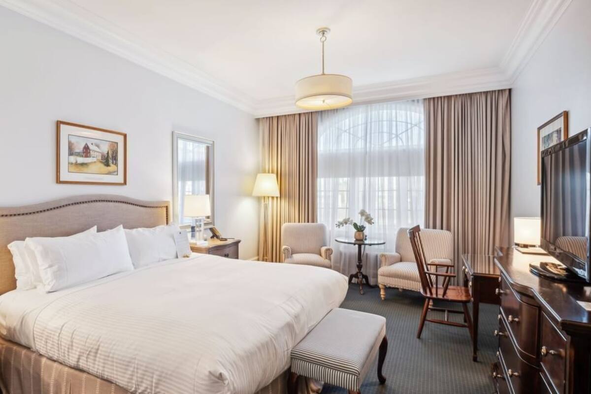 A hotel room with a large bed, a desk, a chair, a television, and a window with curtains.