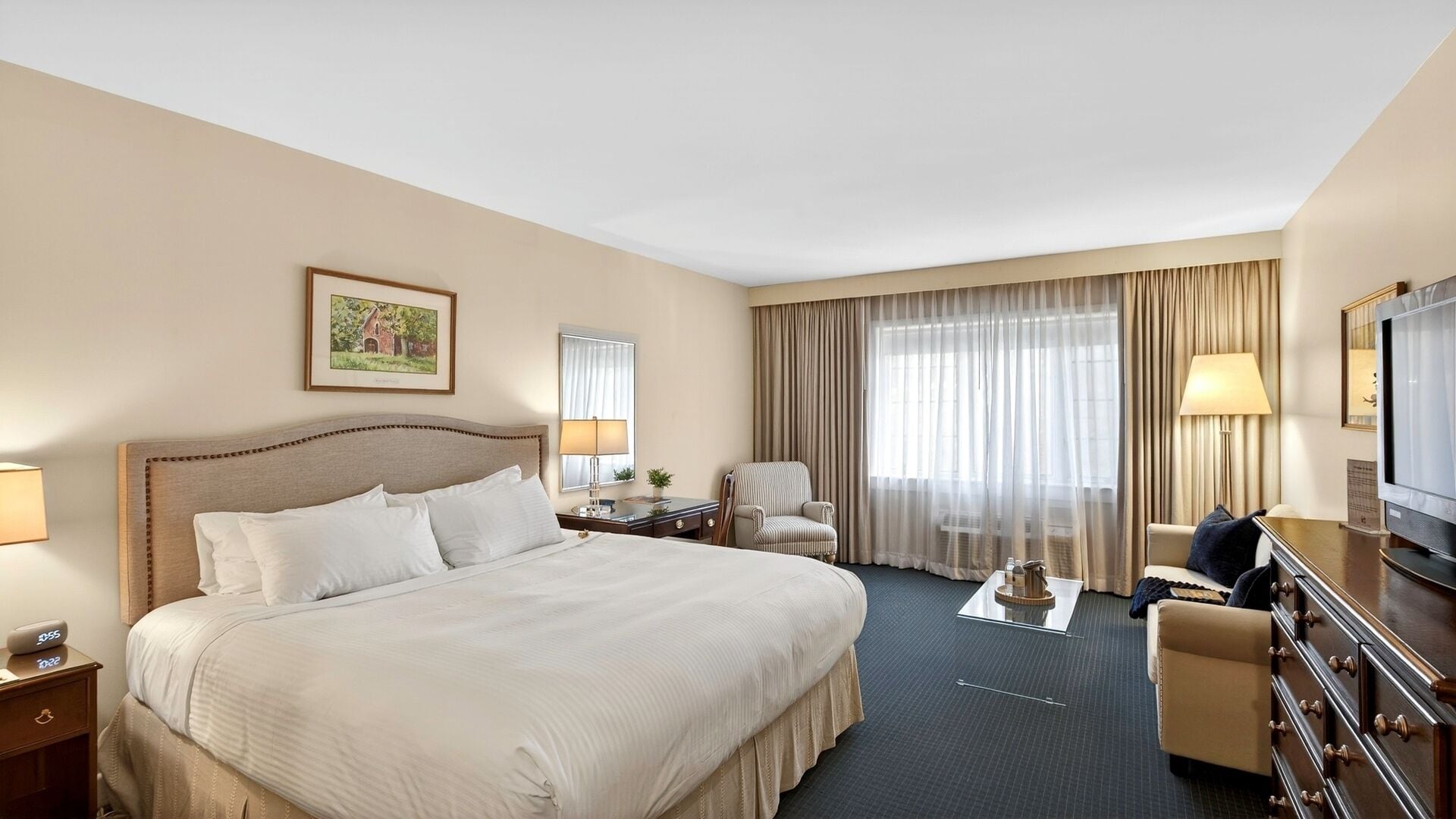 A hotel room with a large bed, a desk, a chair, a TV, and a window with curtains.