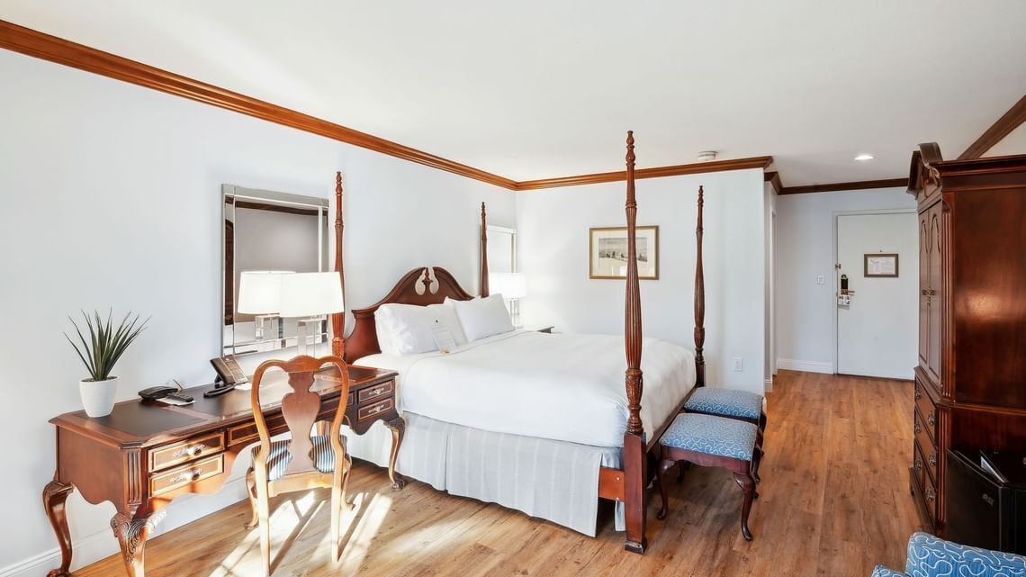 Un lit à baldaquin avec une tête de lit en bois, un bureau avec une lampe, une chaise et un meuble de rangement.