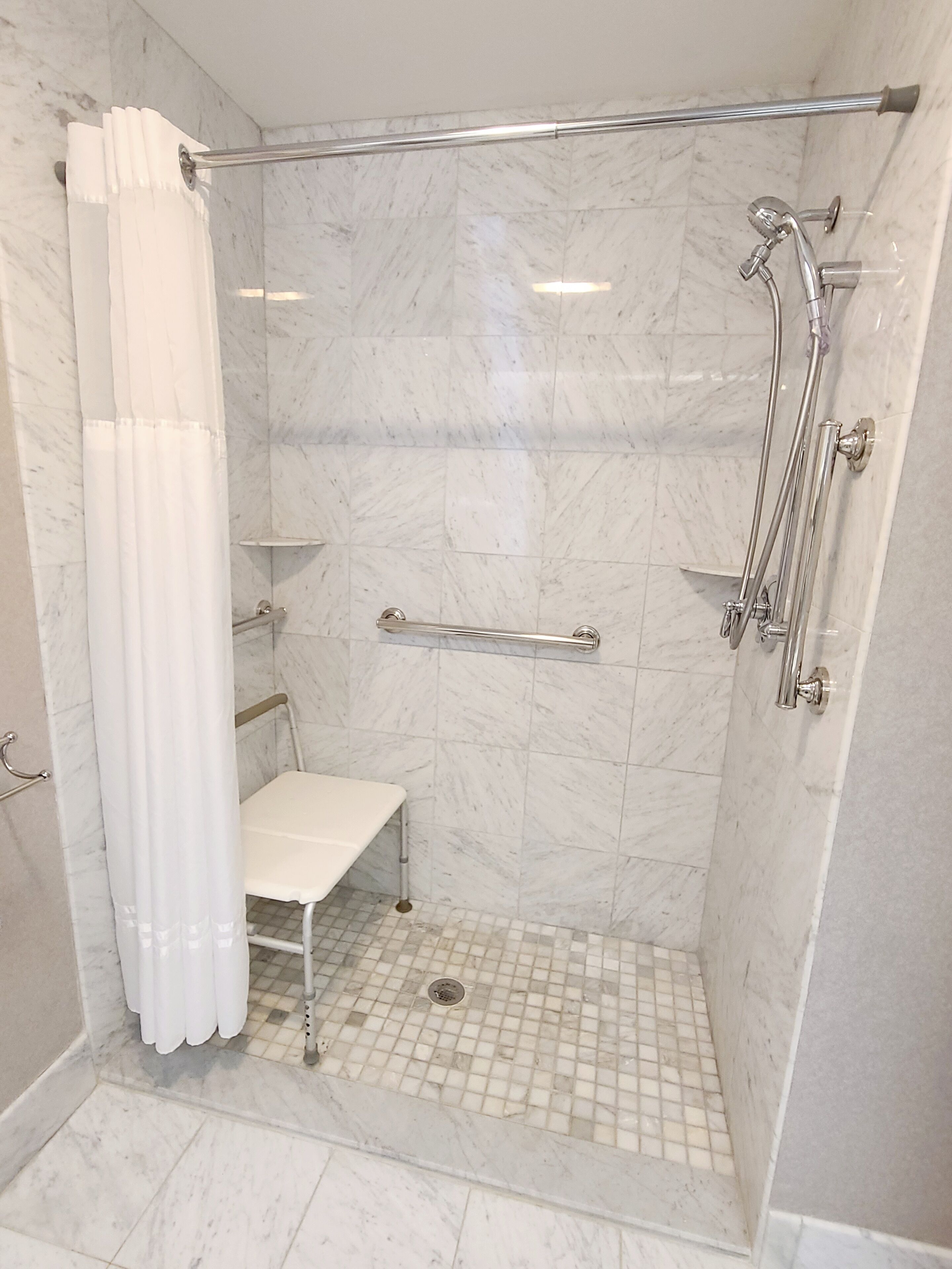A walk-in shower with a white tiled floor, a white bench, and a glass door.