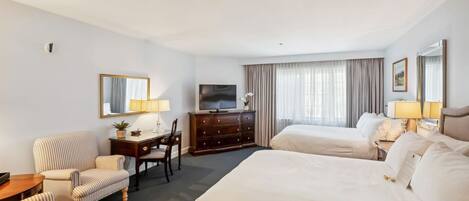 A hotel room with two beds, a desk, a chair, a TV, and a large window with curtains.