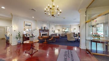 Un amplio vestíbulo de hotel con candelabro, zonas de estar y mostrador de recepción.