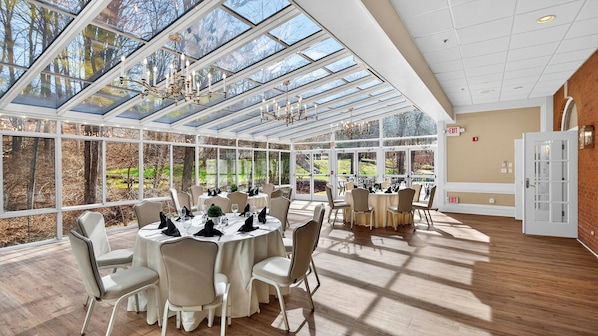 A conservatory with a glass ceiling, round tables, and chairs, and a brick wall with an exit sign. - Avon Old Farms Hotel (Avon)