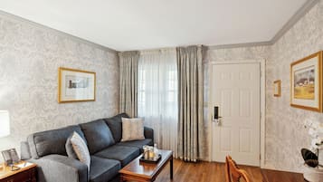 A living room with a dark grey sofa, a wooden coffee table, a desk with a telephone, and a door with a white frame.