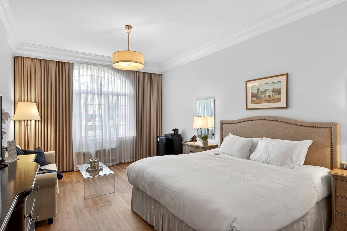A hotel room with a large bed, a desk with a computer, a television, and a window with curtains.