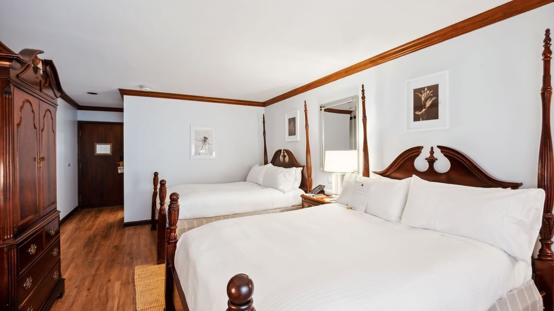 A hotel room with two beds, wooden headboards, a wardrobe, and a mirror.