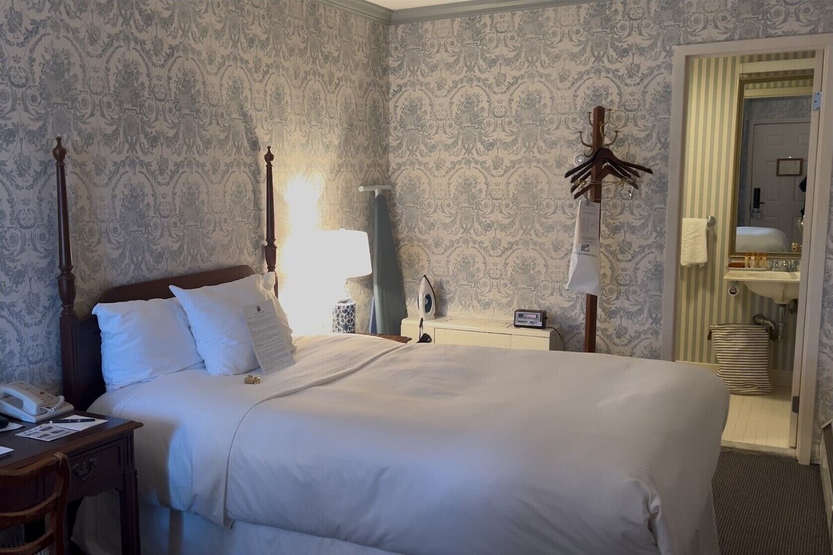 A hotel room with a large bed, a bedside table with a lamp, a mirror, and a wardrobe.