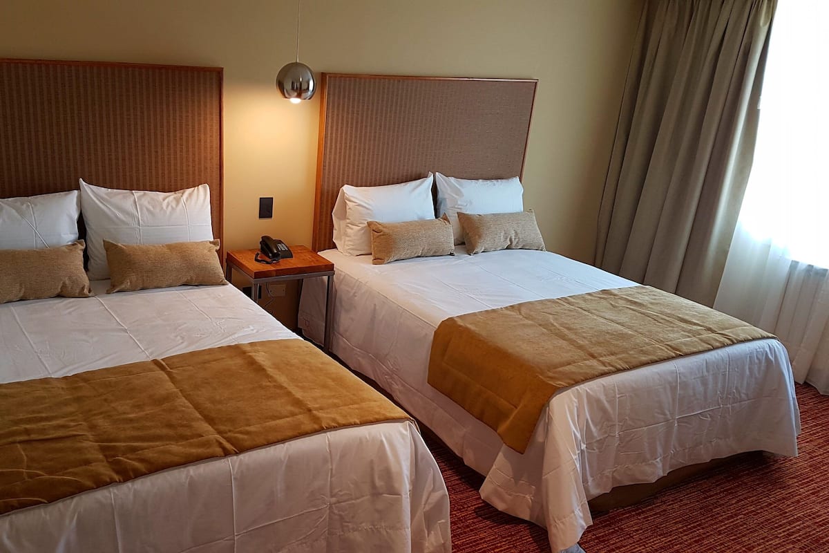 Habitación de hotel con dos camas, una mesita de noche con teléfono y una ventana con cortinas.