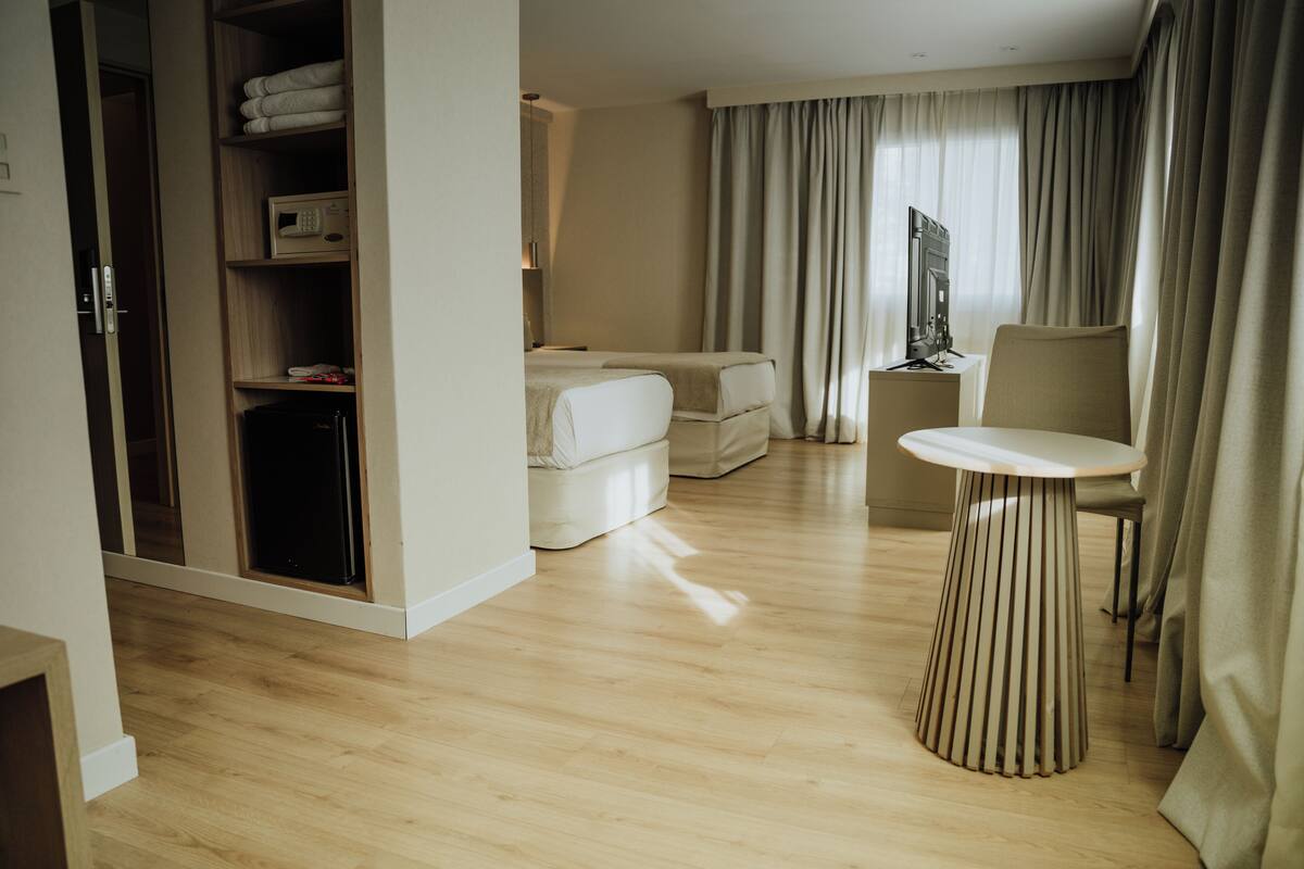 A hotel room with a wooden floor, a bed, a seating area with a table, and a wardrobe.
