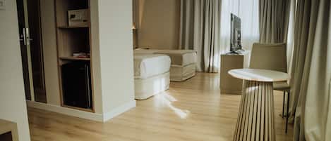 A hotel room with a wooden floor, a bed, a seating area with a table, and a wardrobe.