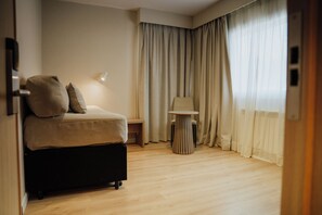 A hotel room with a bed, a small table, a lamp, and curtains.