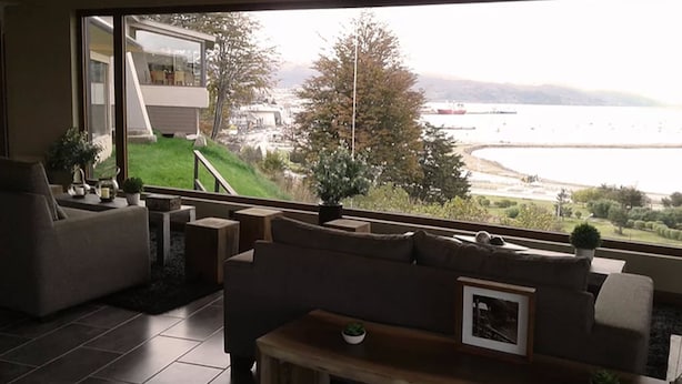 A modern living room with a large window overlooking a scenic view of a body of water and hills. - Las Lengas Hotel (Ushuaia)