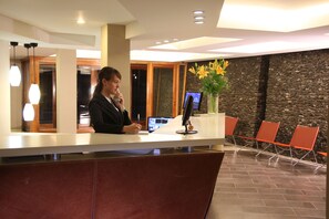 A reception desk with a monitor, a vase with flowers, and a seating area with chairs.