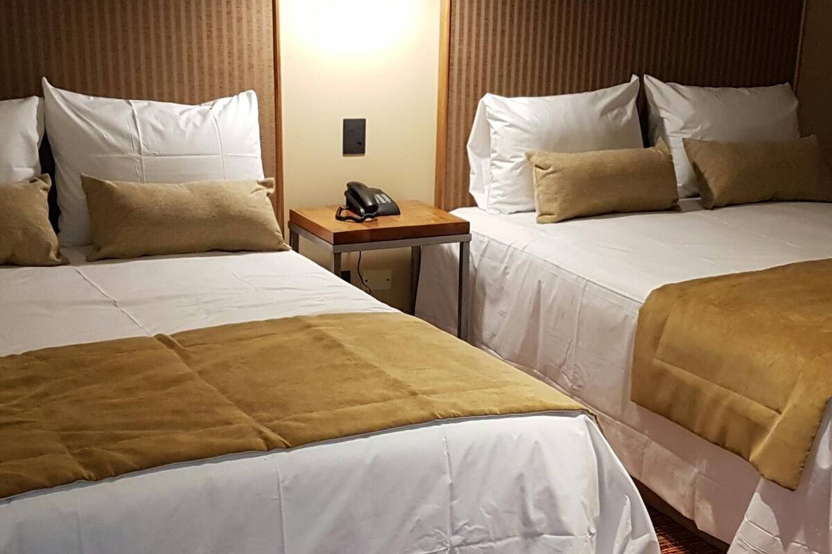 A hotel room with two beds, a desk with a phone, and a wall-mounted light.