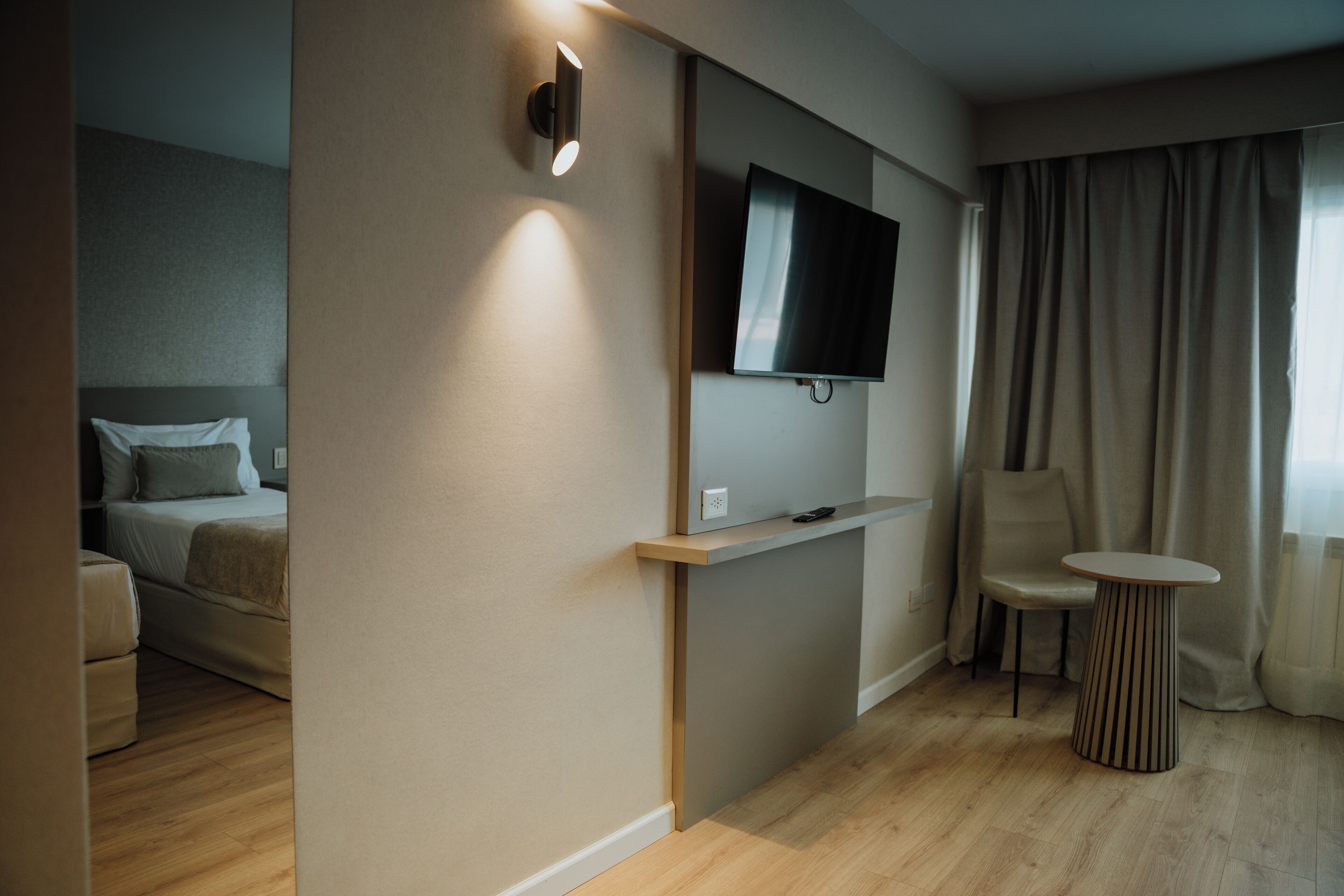 A modern hotel room with a bed, a TV mounted on the wall, a small table, and a chair.