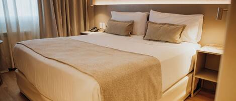 A neatly made bed with a beige blanket, a bedside table with a lamp, and a phone on the nightstand.