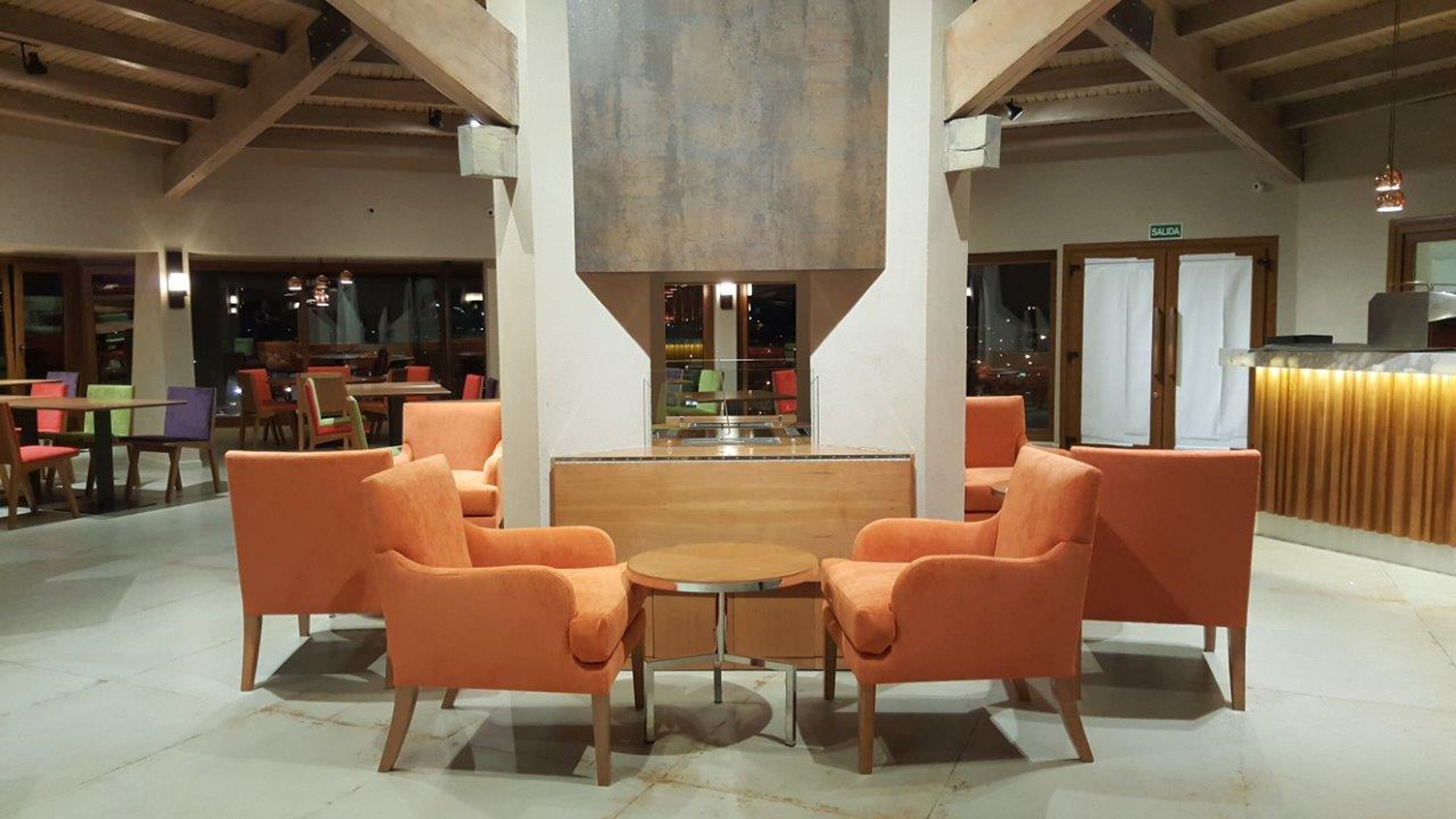 Un hall d’entrée spacieux avec de hauts plafonds, un espace salon central avec des fauteuils orange et un comptoir de réception bien visible.