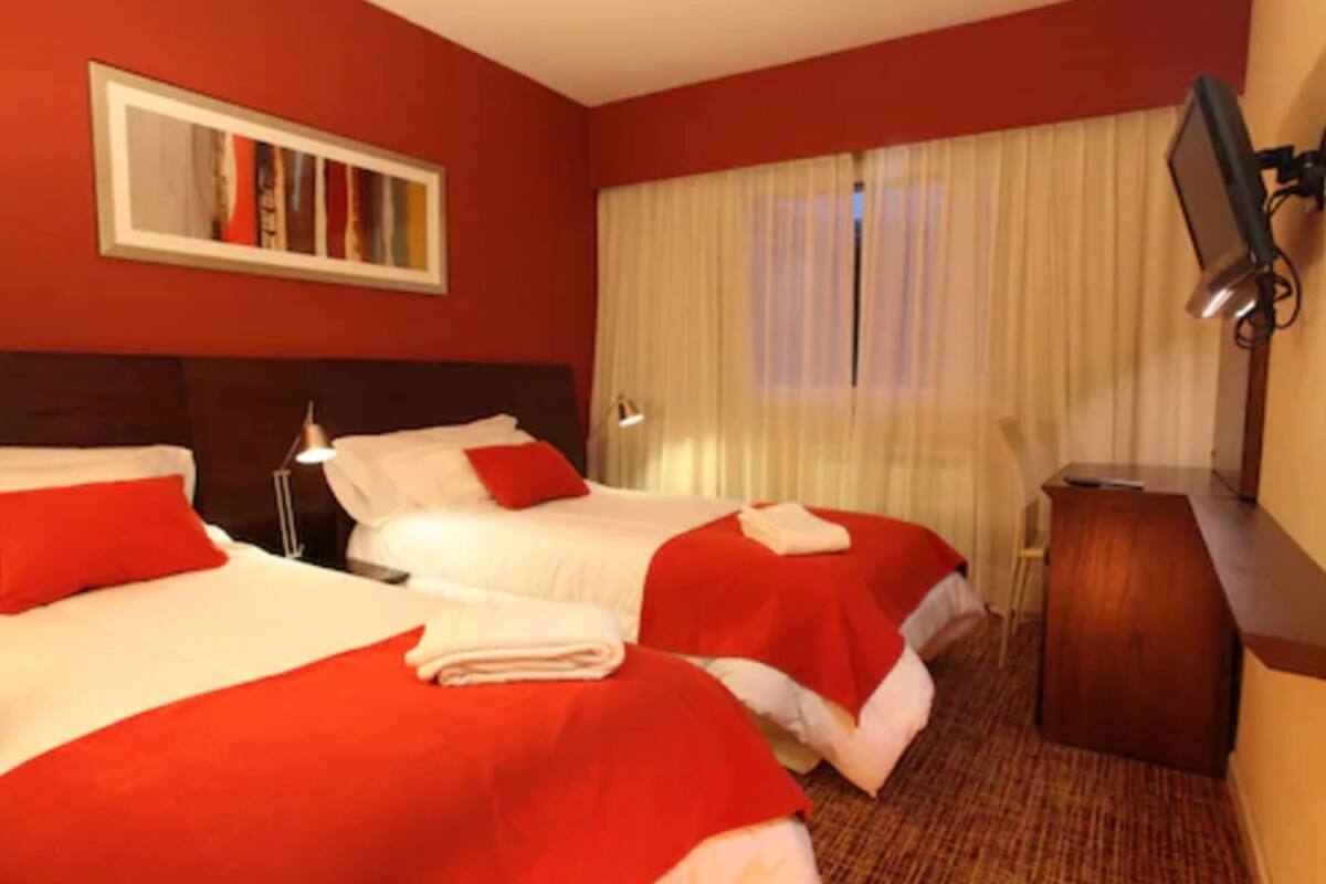 A hotel room with two beds, a desk, a TV, and a window with curtains.