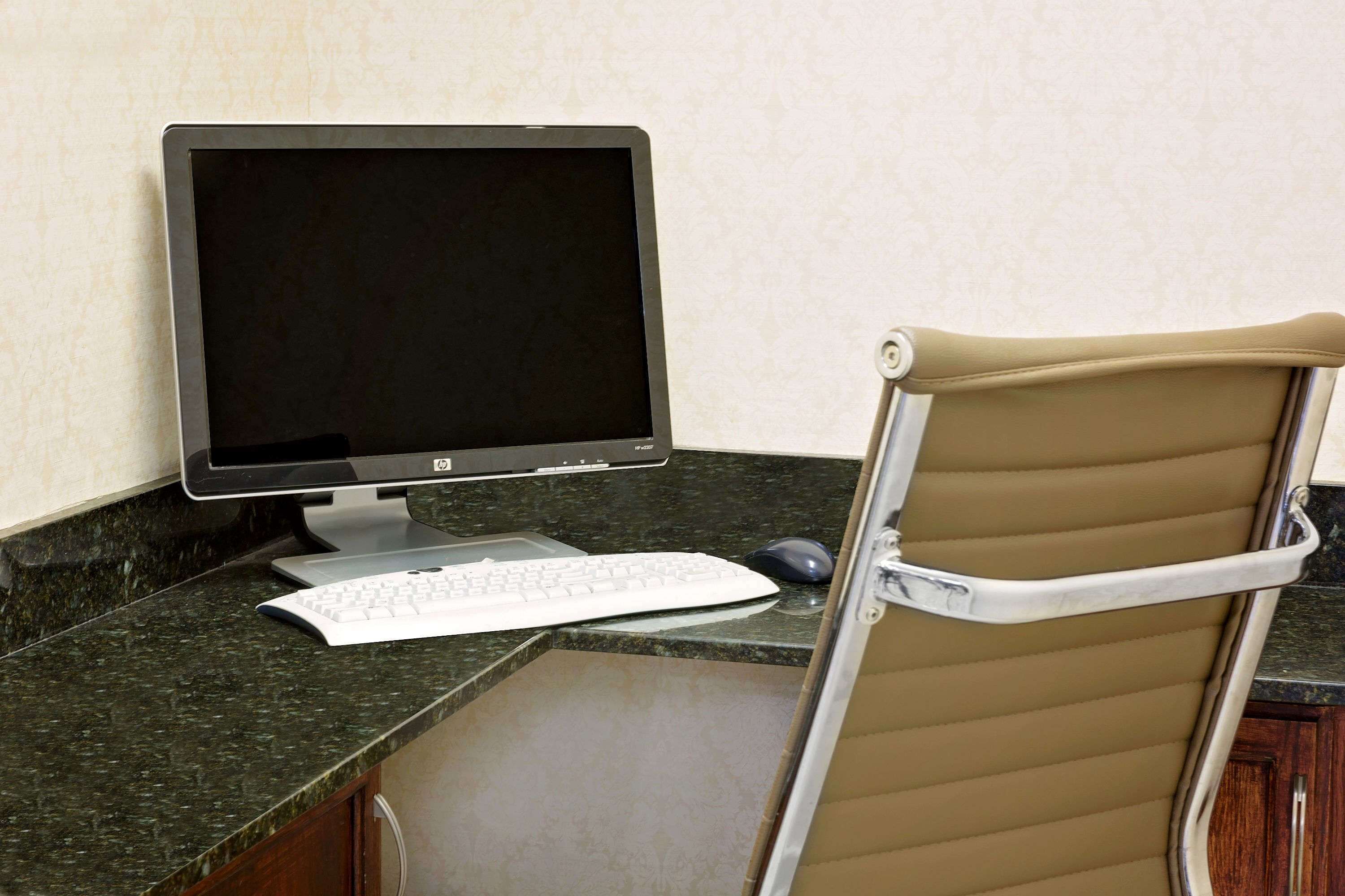 A corner office with a desktop computer, a keyboard, and a mouse on a granite countertop.