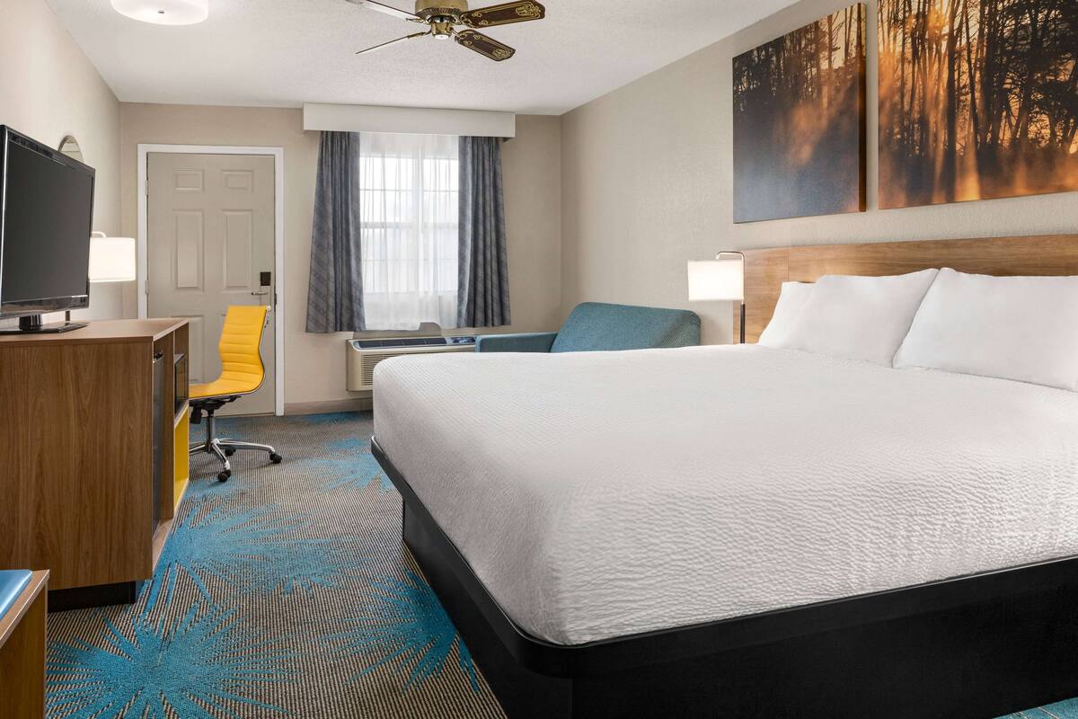 A hotel room with a large bed, a desk with a computer, a television, and a chair.