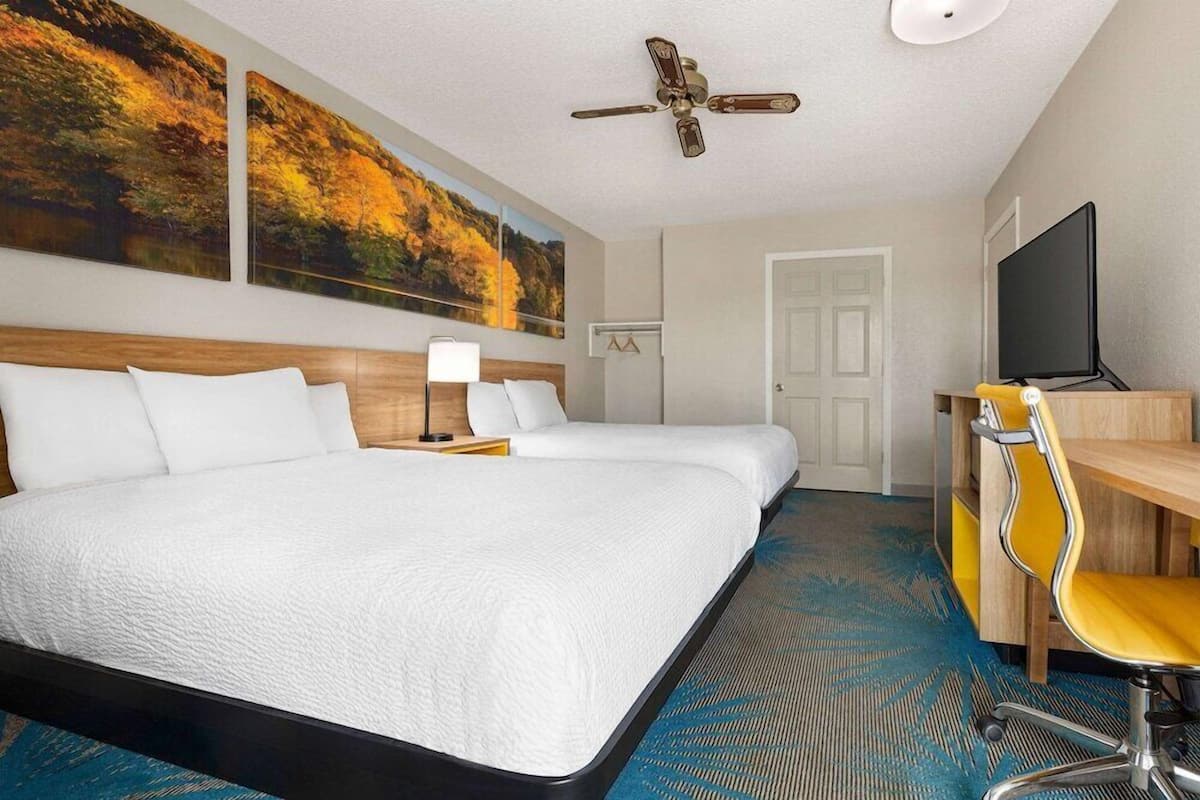 A hotel room with a large bed, a desk with a chair, a television, and a ceiling fan.