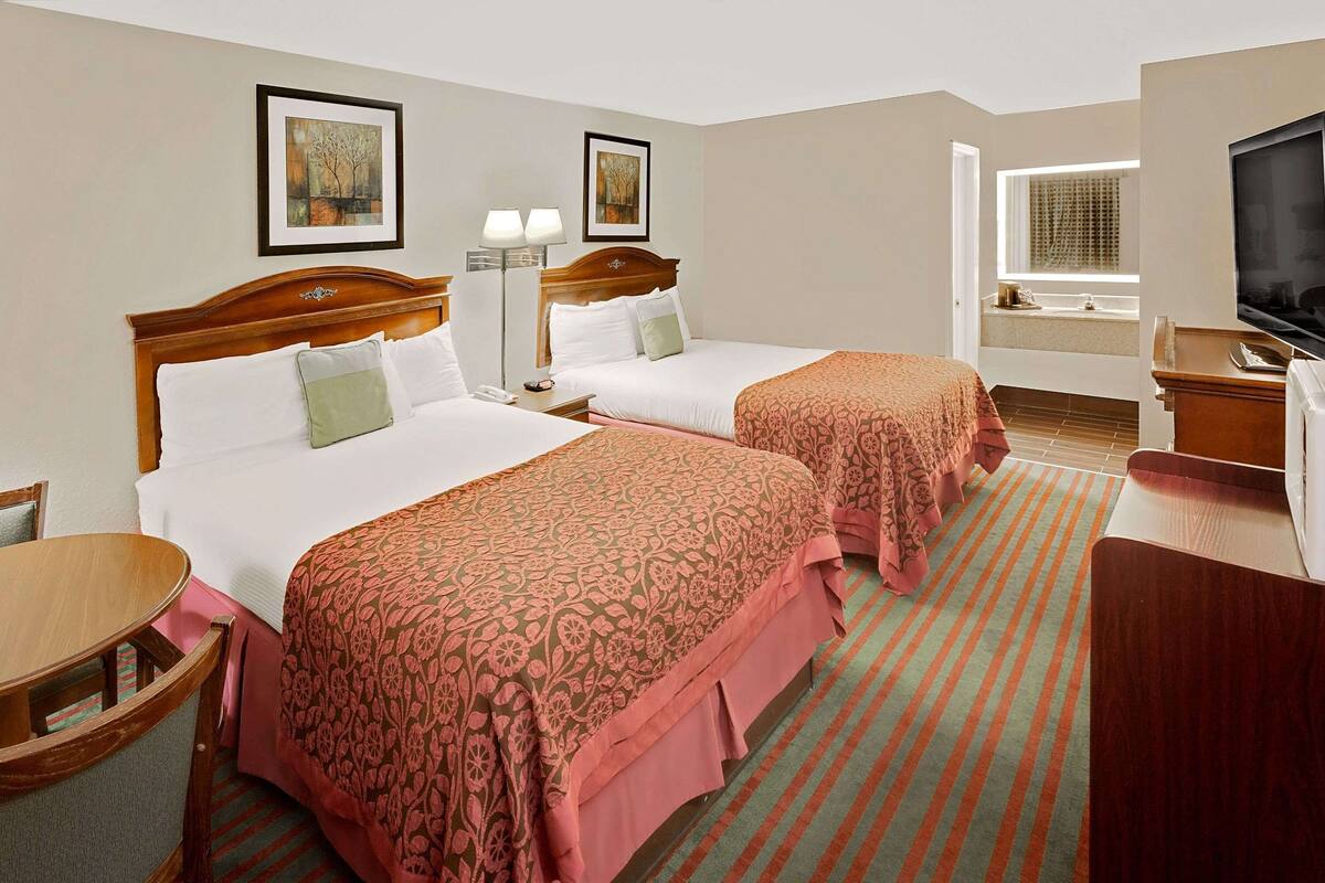 A hotel room with two beds, a TV, a desk, and a bathroom with a window.