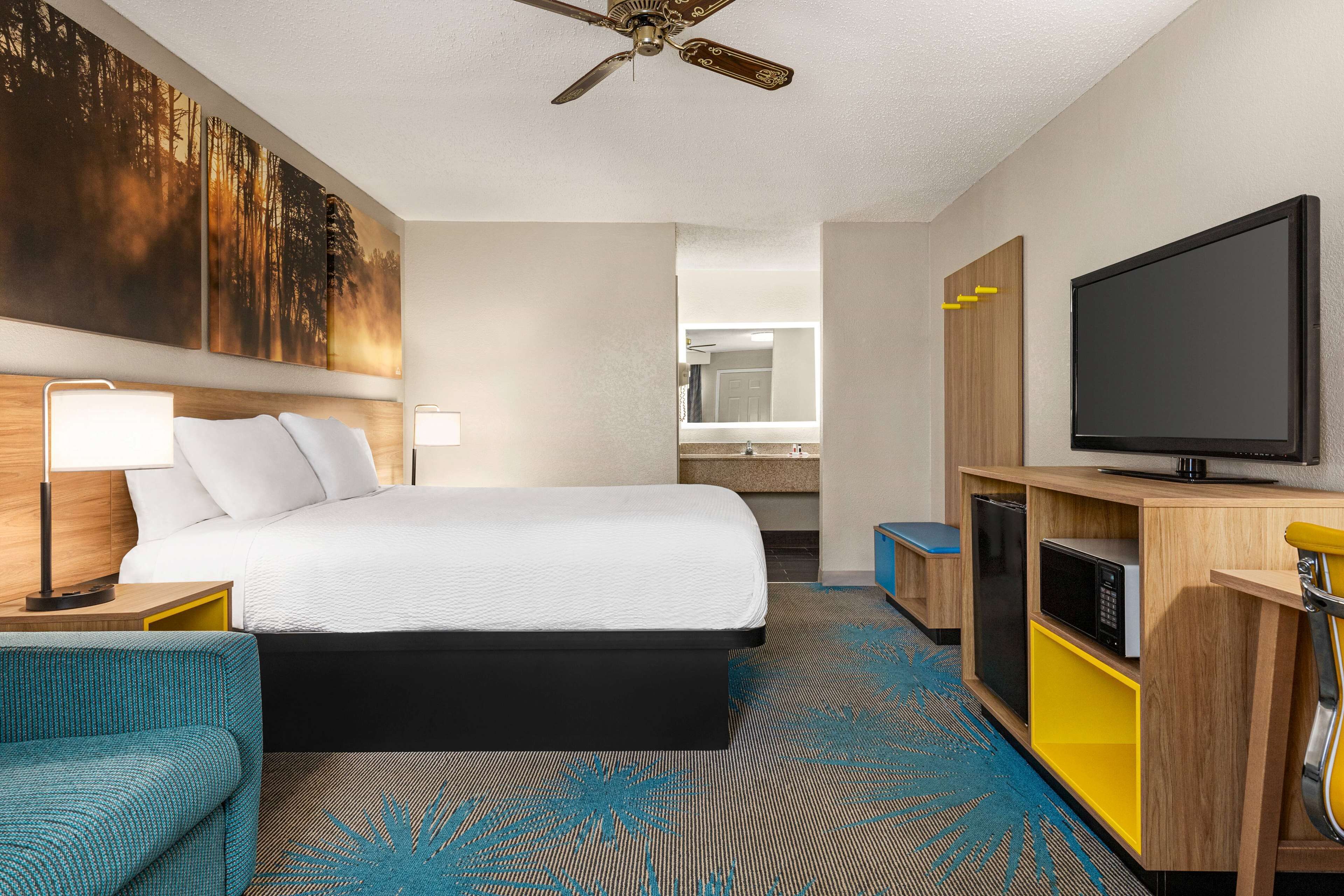 A hotel room with a bed, a desk with a lamp, a television, a microwave, and a large painting on the wall.