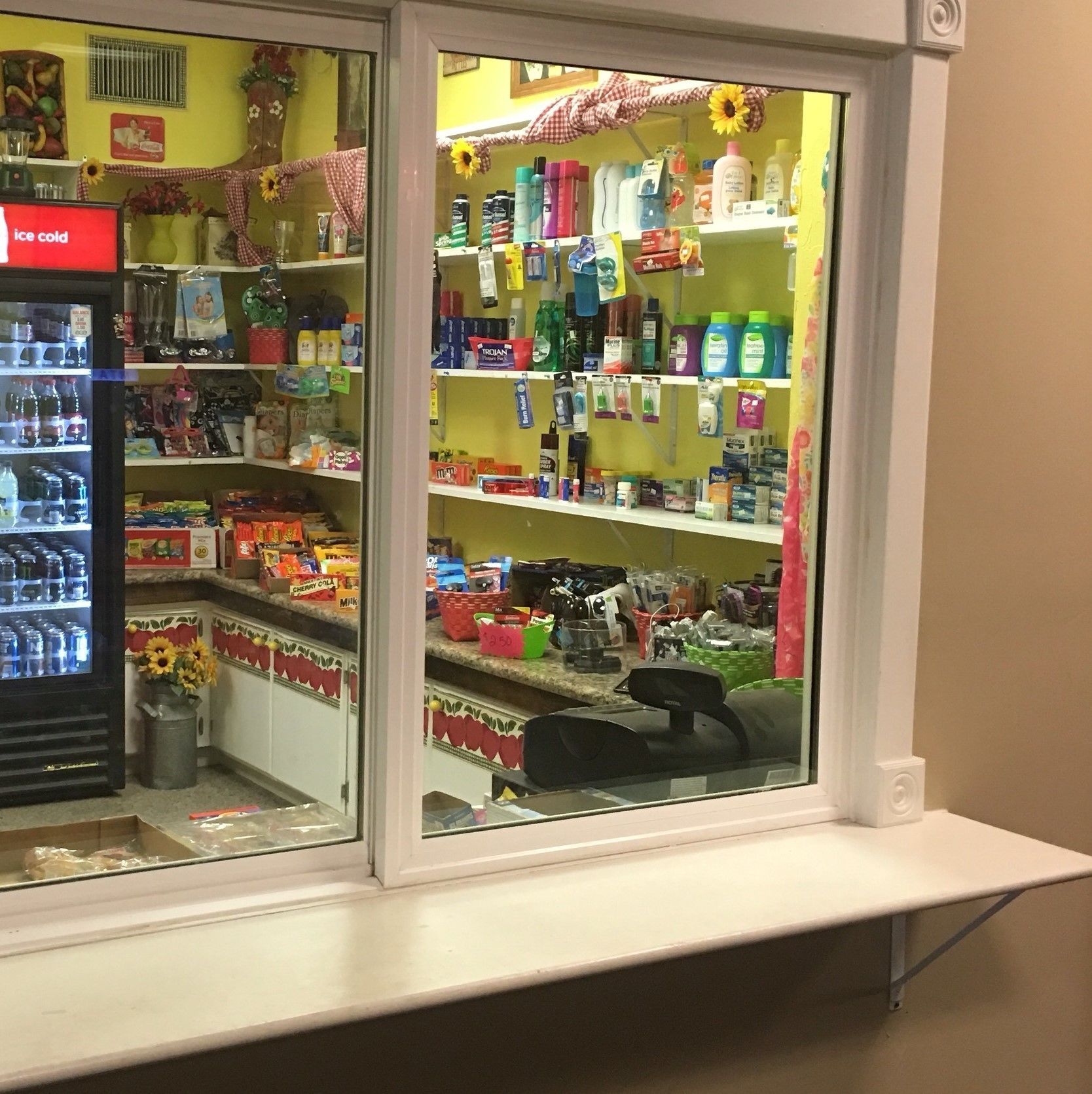 A store with shelves stocked with various products, a refrigerator with beverages, and a window display with sunflowers.