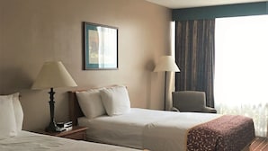 A hotel room with two beds, a chair, a lamp, and a window with curtains.