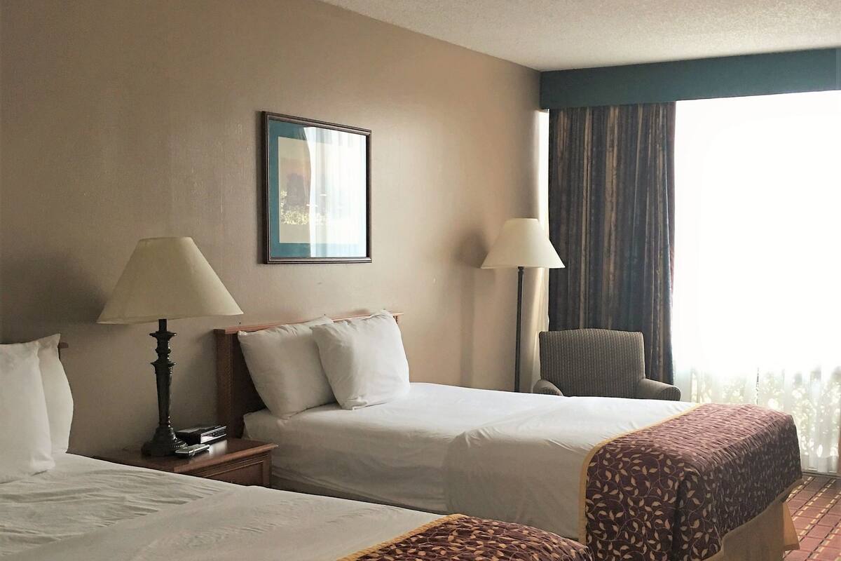 A hotel room with two beds, a chair, a lamp, and a window with curtains.