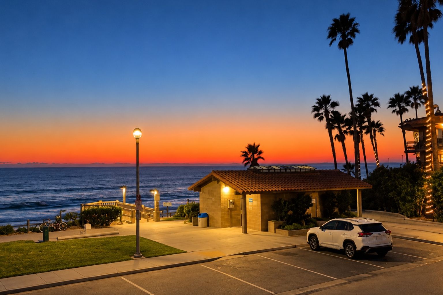 Un hôtel situé sur la côte, doté d’un parking, d’un petit bâtiment avec un toit en tuiles et offrant une vue sur l’océan au coucher du soleil.