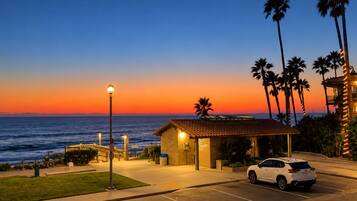 Un hôtel situé sur la côte, doté d’un parking, d’un petit bâtiment avec un toit en tuiles et offrant une vue sur l’océan au coucher du soleil.