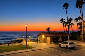 Hotel à beira-mar com estacionamento, um pequeno edifício com telhado de telhas e vista para o oceano ao pôr do sol.
