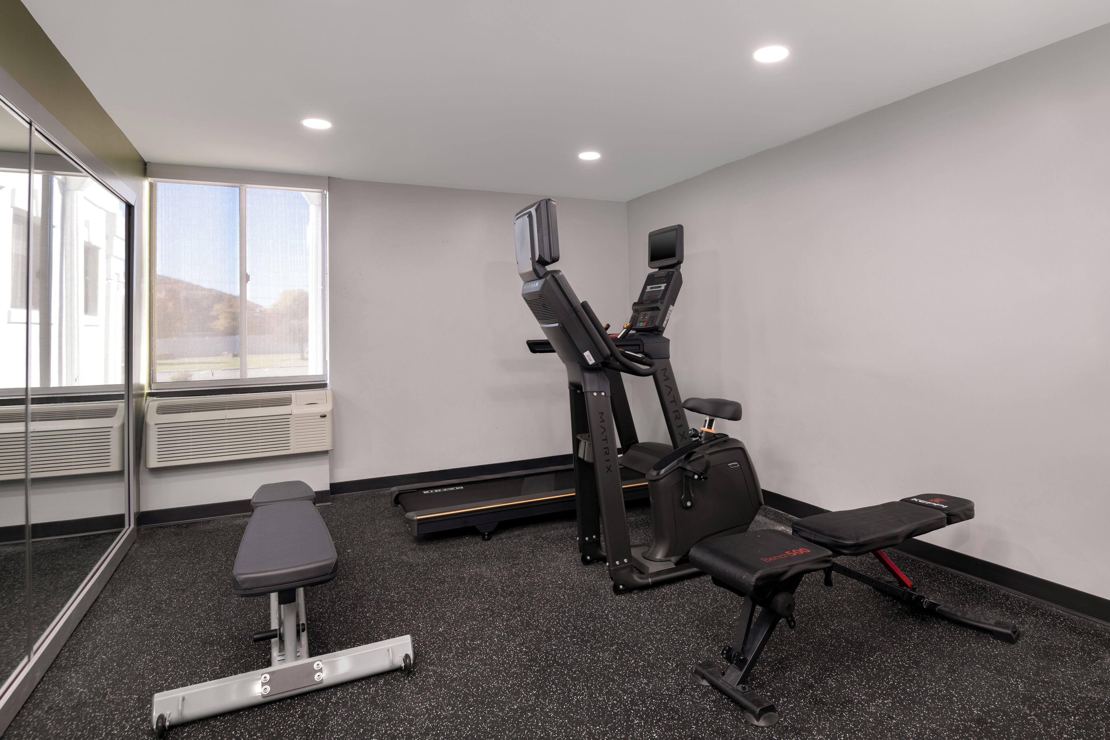 A gym with a treadmill, bench, and weight machine.