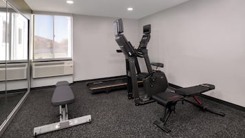 A gym with a treadmill, bench, and weight machine.