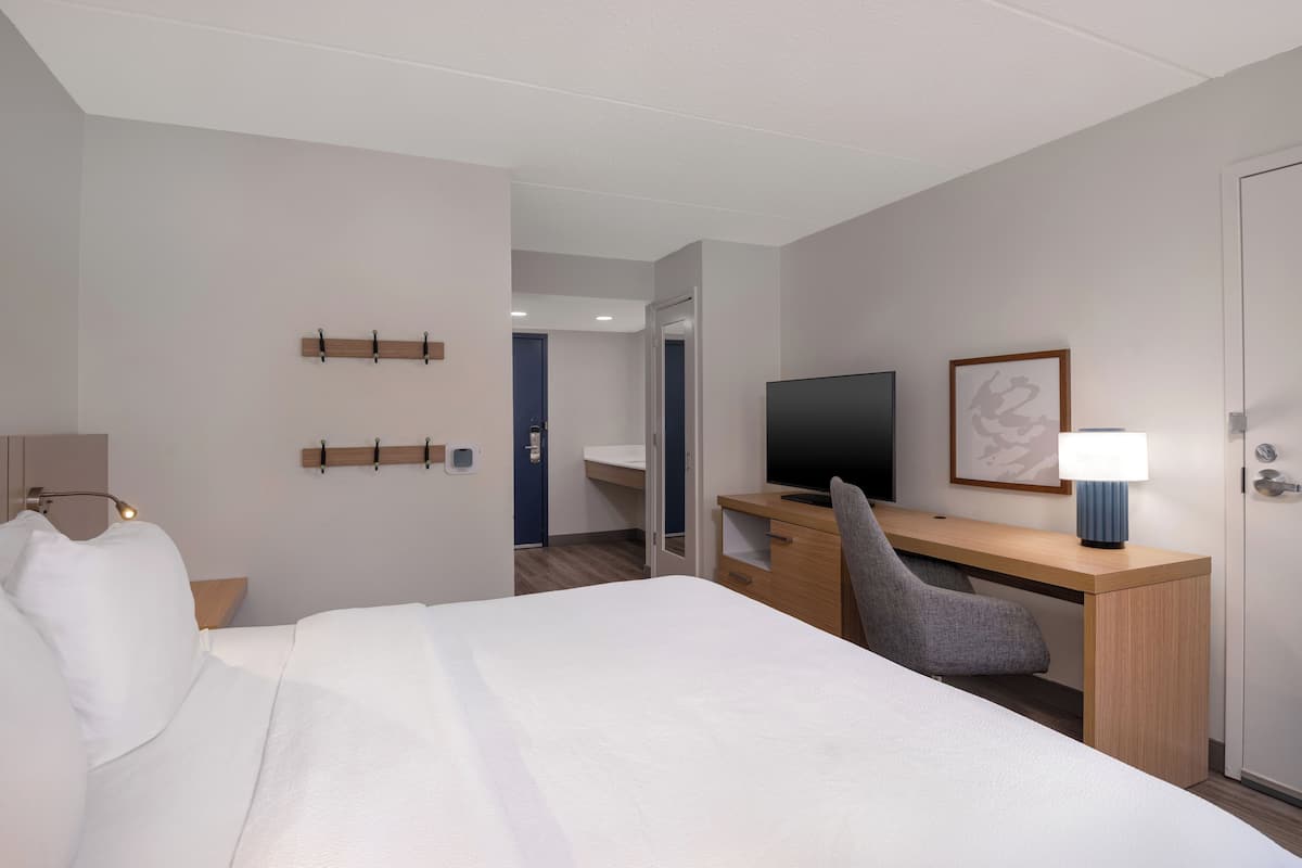Hotellihuone, jossa on sänky, työpöytä, tuoli, televisio, lamppu ja ovi.